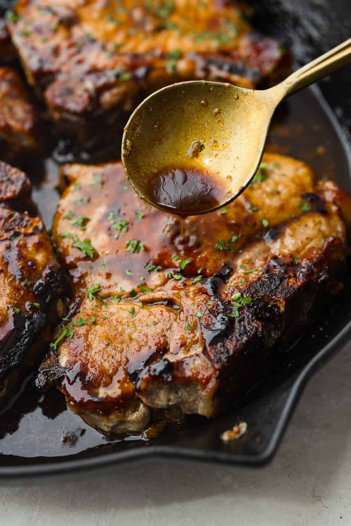 Close up shot of someone pouring glaze over pork chop. 