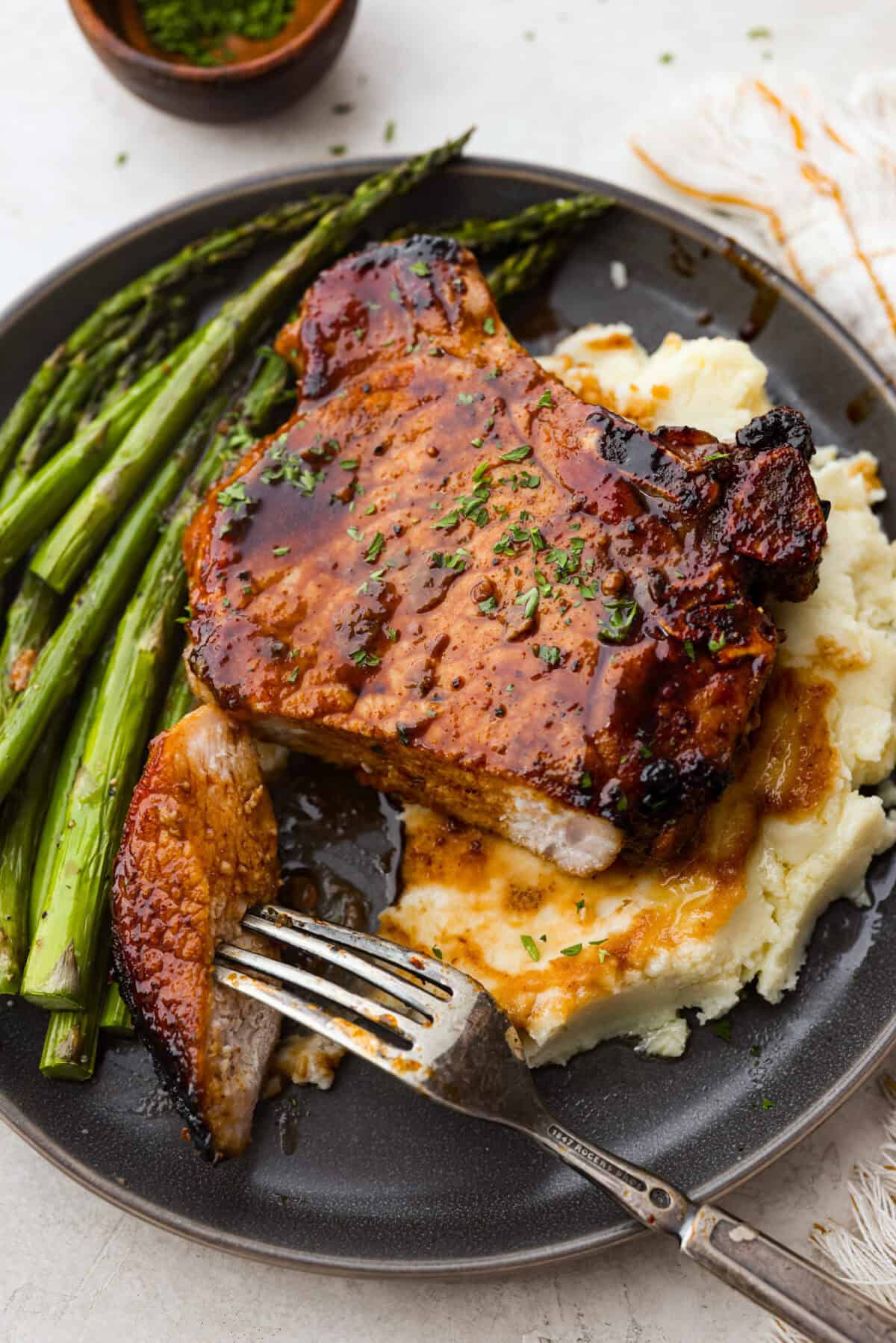 Angle shot of plated pork chop over mashed potatoes, next to asparagus. 