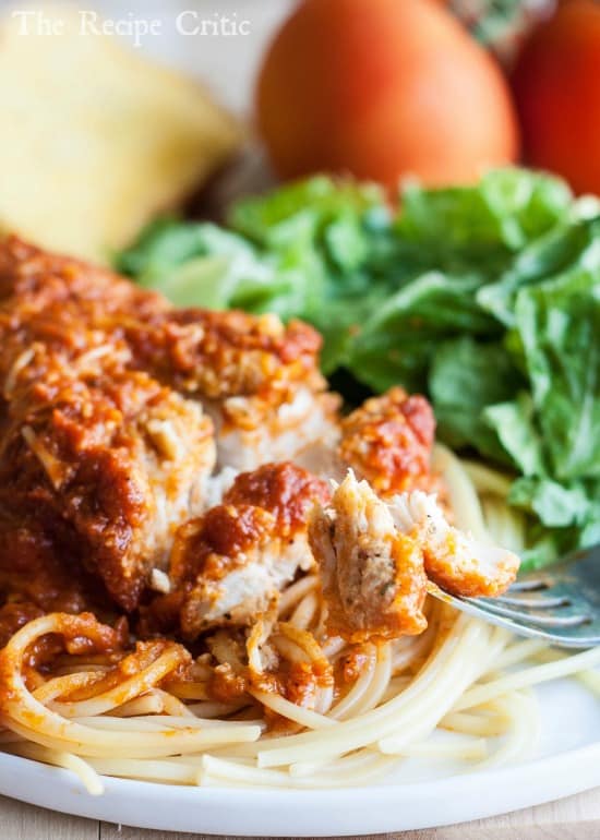 Slow Cooker Chicken Parmesan over spaghetti on a white plate with green salad in the background. 