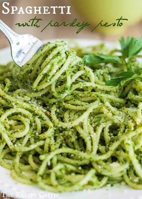 Spaghetti noodles with parsley pesto sauce on a white plate with a fork twirling noodles.