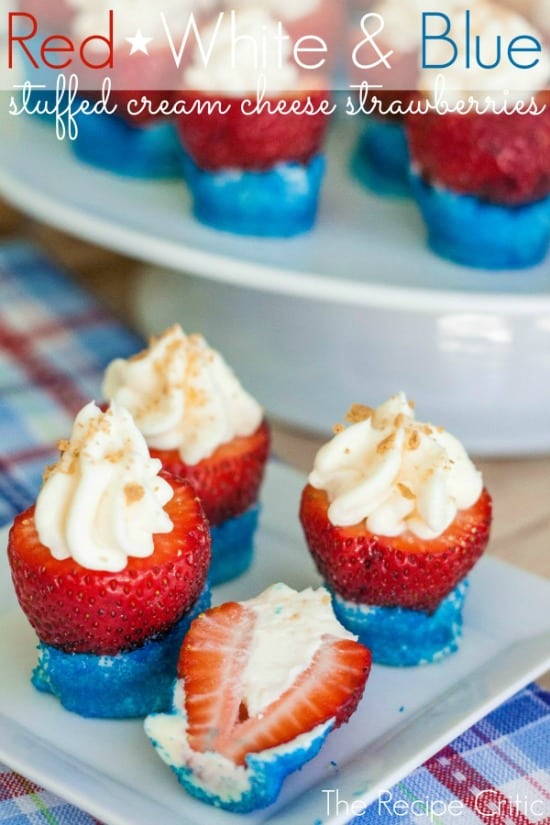 Red white and blue stuffed cream cheese strawberries on a white cake stand and white plate.