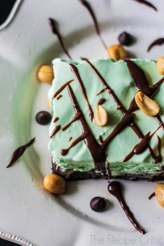 Frozen mint brownie square drizzled with chocolate and garnished with peanuts on a white plate.
