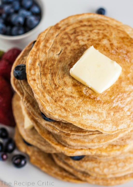 Stack of 8 pancakes with butter and blueberries between layers.