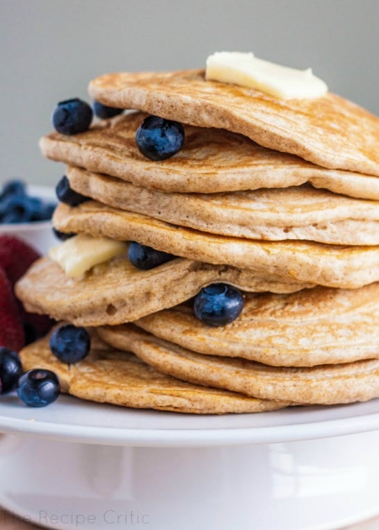 Stack of 8 pancakes with blueberries and butter between layers on a white plate.