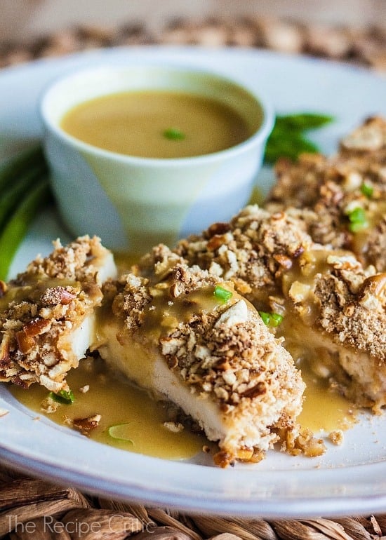 Honey Mustard Chicken cut into strips on a white plate and drizzled with honey mustard, with a side dish of honey mustard on the plate.