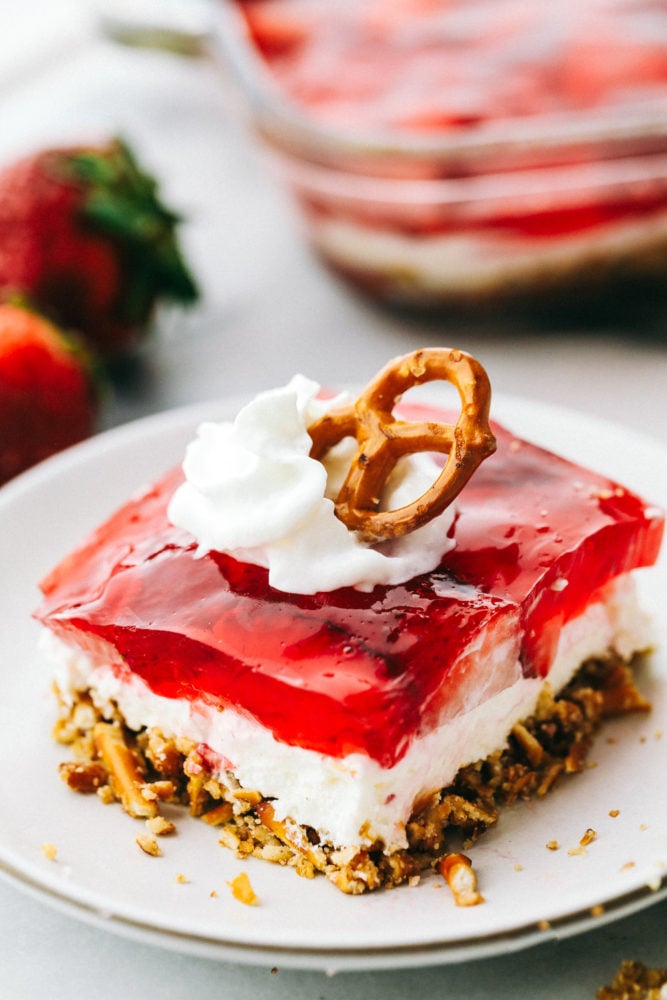 Strawberry Pretzel salad square with a dollup of whip and a pretzel on top.