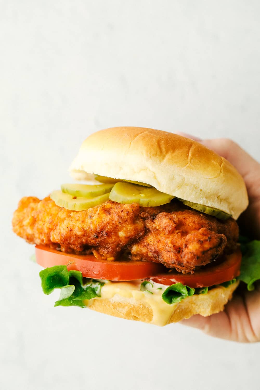 Holding a chicken sandwich with pickles, lettuce and tomatoes. 