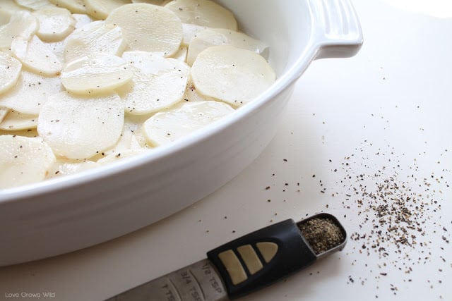 Potato slices in a white baking dish by Love Grows Wild for The Recipe Critic