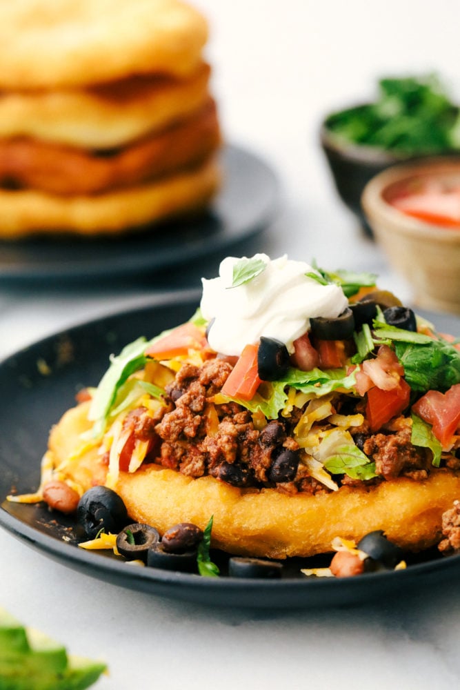 Taco de navajo en un plato con frijoles, tomates de carne molida, lechuga, queso y crema agria.