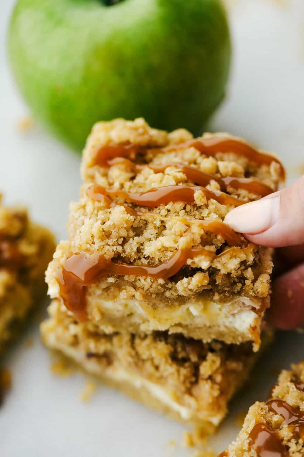 A caramel apple cheesecake bar being held with a hand. 