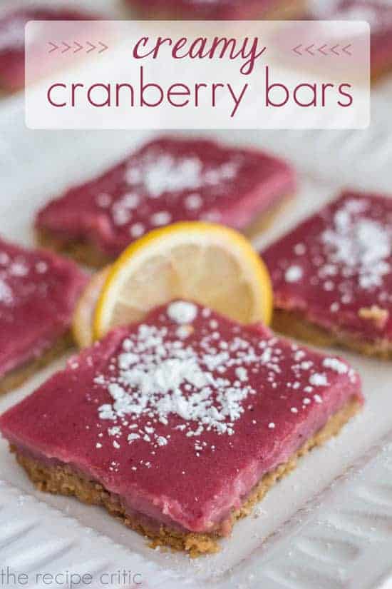 Creamy cranberry bar squares on a white cloth with powered sugar on top and a slice of lemon for garnish.