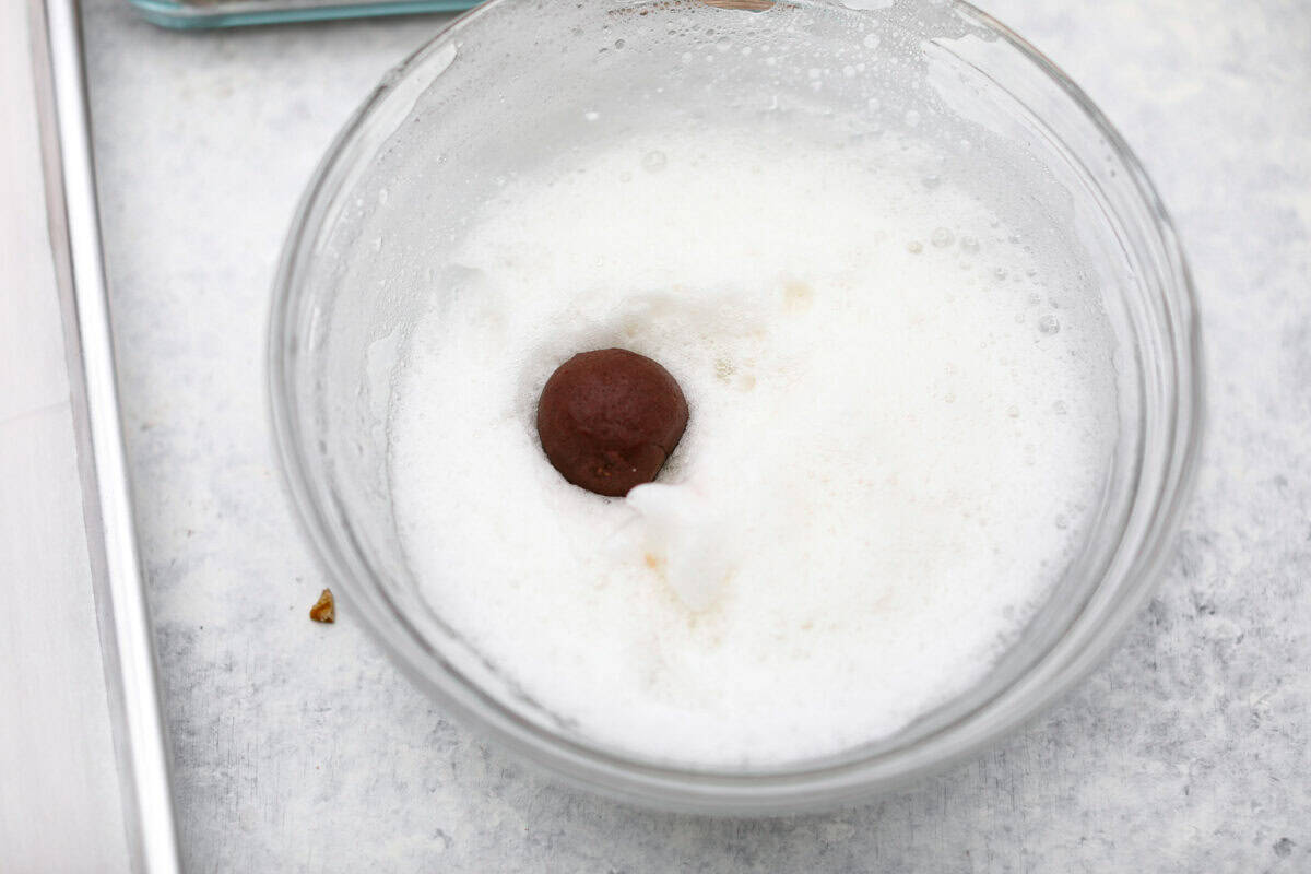 Overhead shot of a turtle cookie dough ball in the bowl of whipped egg whites.