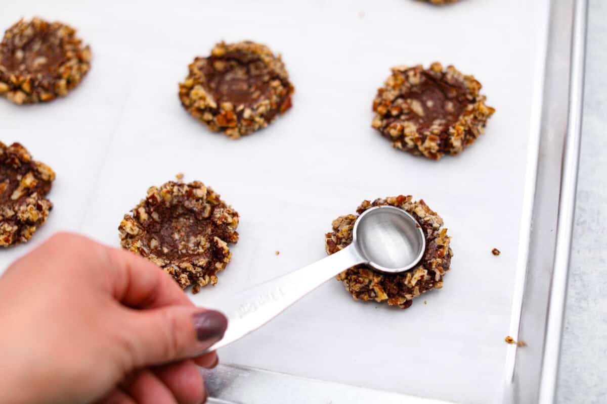 Angle shot of someone making indents in the cookie dough balls with pecans. 