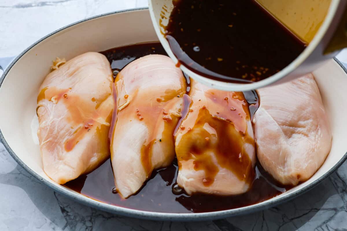 Overhead shot of sauce being poured over chicken breast. 