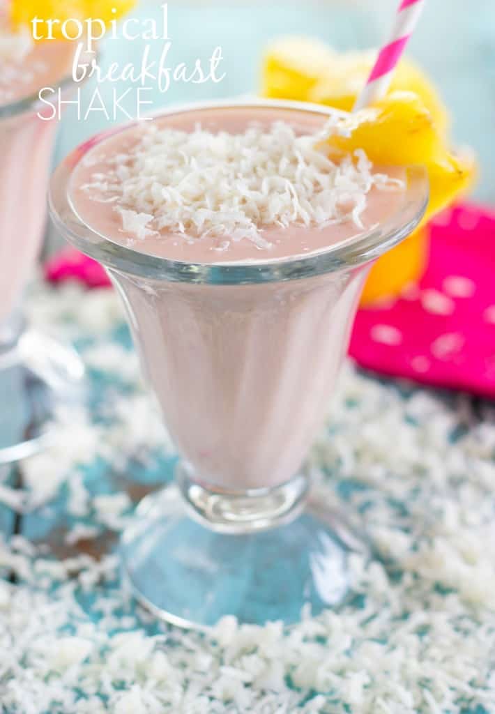 Tropical Breakfast Shake in einem Glasbecher mit einem rosa Strohhalm und Kokosraspeln an der Seite. 
