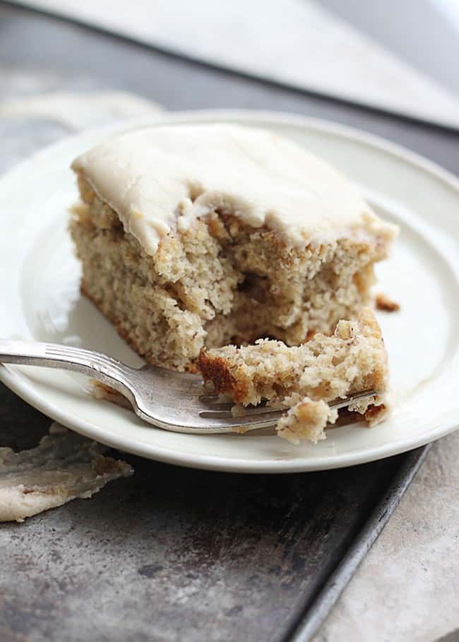 Browned Butter Banana Cake with Brown Sugar Frosting on a white plate with a fork taking a bite out of it. 