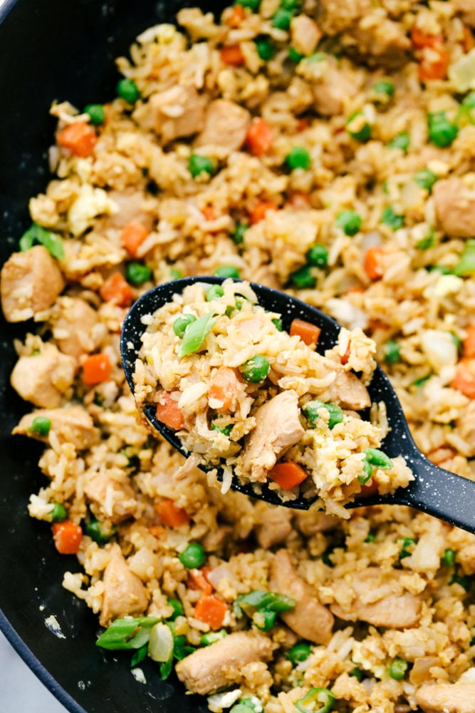 Chicken fried rice in a skillet with a spoon scooping up some to show a zoom in. 