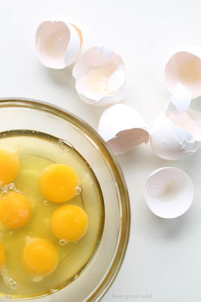 Cracked eggs in a clear mixing bowl. There are egg shells on the side of the bowl. 