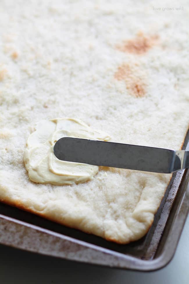 A spread is being applied to the top of the pizza crust. 