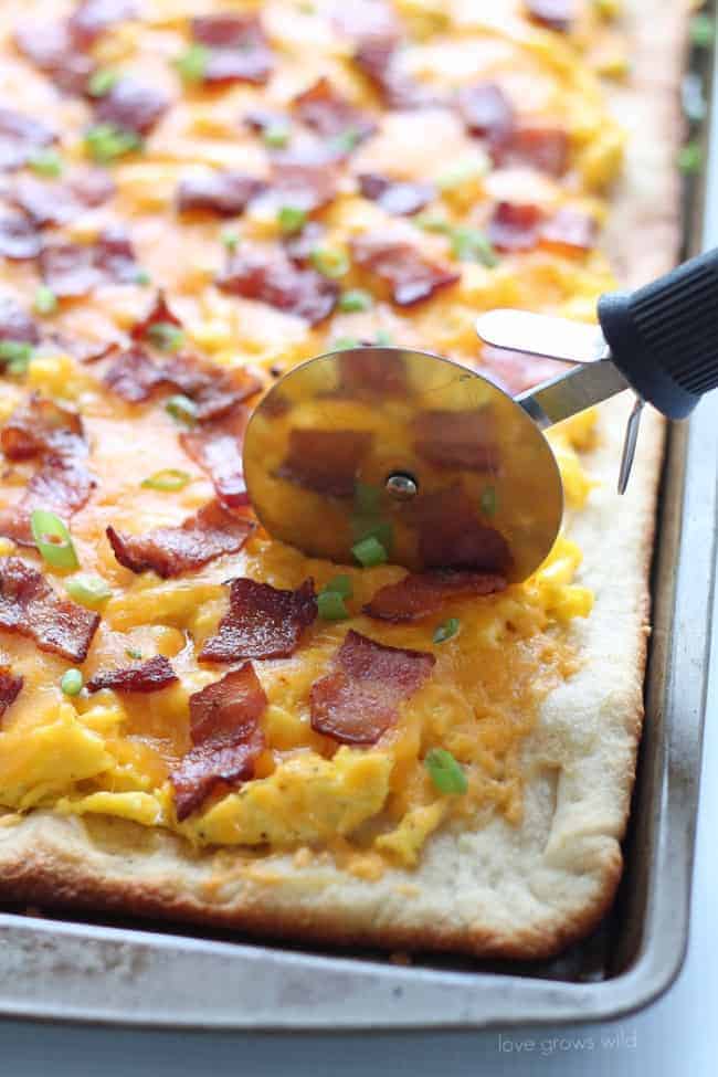 A pizza slicer, slicing into Bacon and Cheddar Breakfast Pizza. 