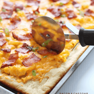 The perfect breakfast pizza topped with soft scrambled eggs, crispy bacon, and lots of melty cheddar cheese!