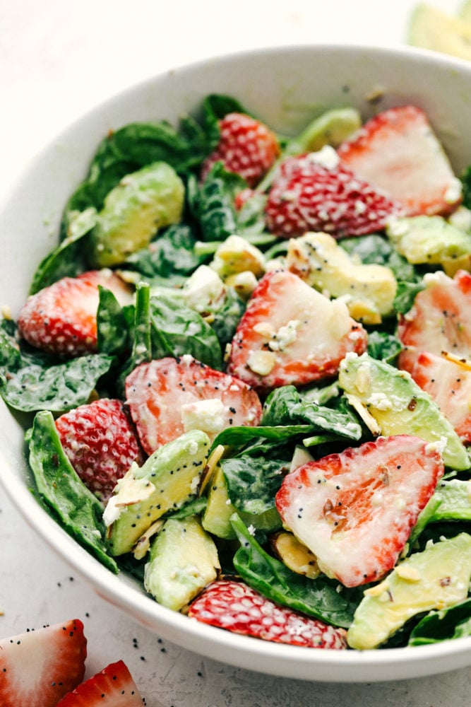 Ensalada de espinacas con aguacate y fresas mezcladas en un tazón blanco y listas para servir. 