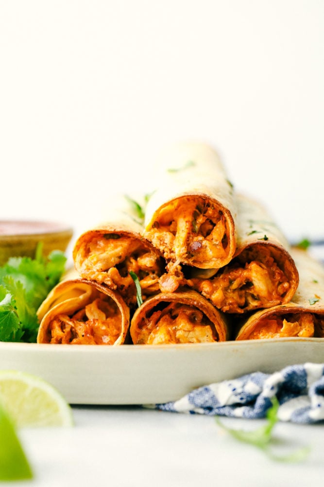 Les taquitos au poulet au fromage à la crème sont empilés les uns sur les autres avec des quartiers de citron vert comme garniture. 