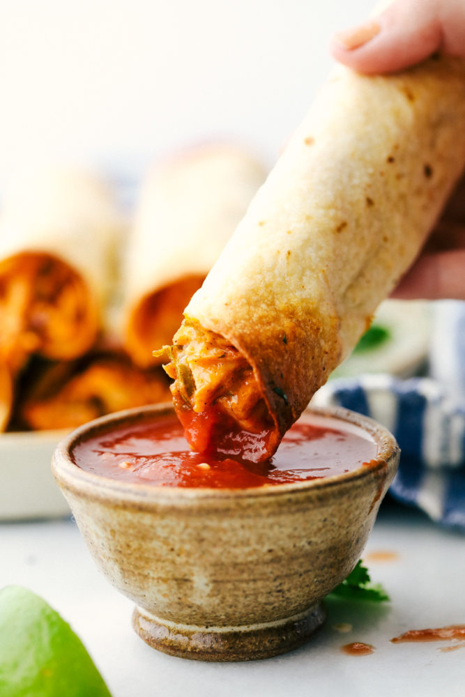 Cream cheese chicken taquito is being dipped in a red salsa. 