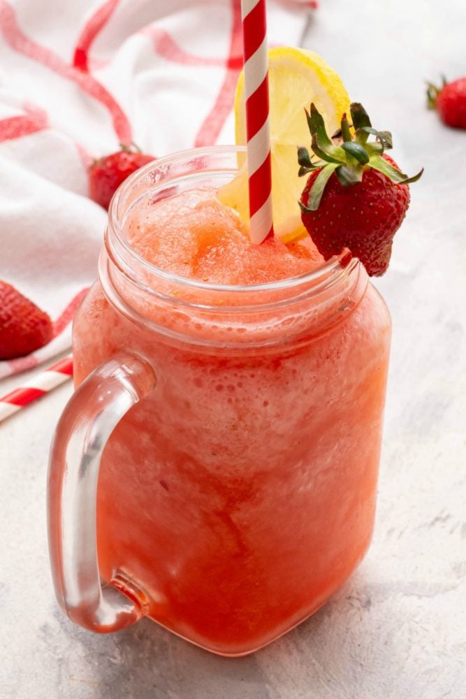 Frozen strawberry lemonade with a straw and lemon wedge. 