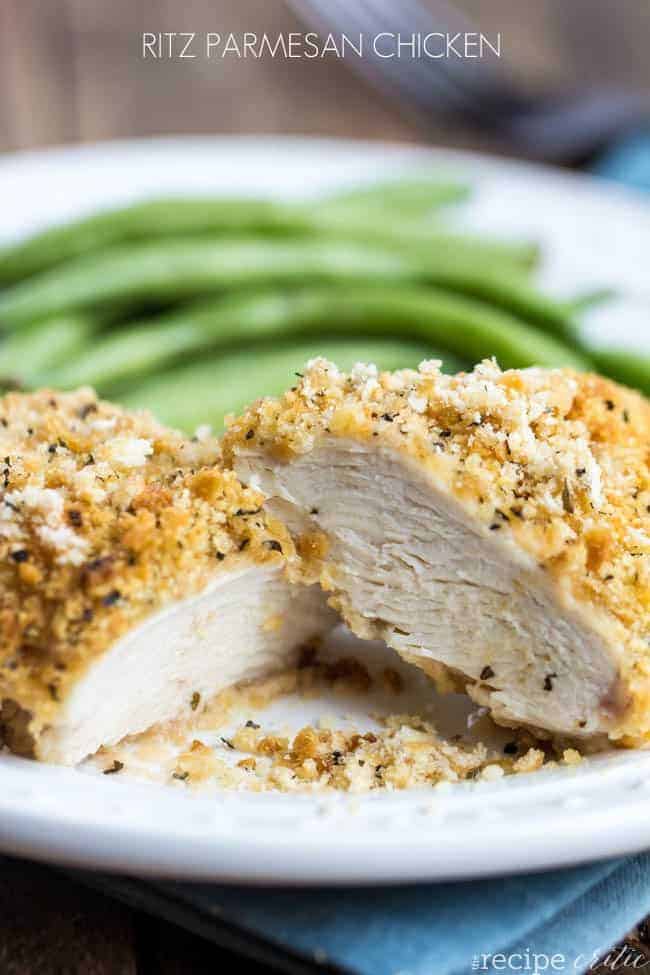 Ritz parmesan chicken cut in half on a white plate with green beans as side dish. 