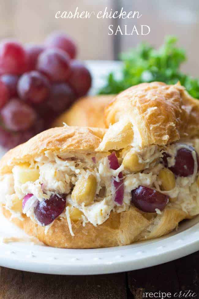 Cashew chicken salad on a bun with grapes in the background. 