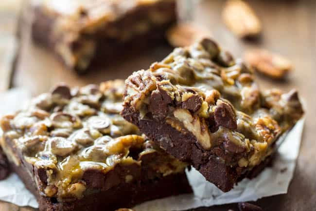 Caramel chocolate pecan bars stacked on top of each other. 