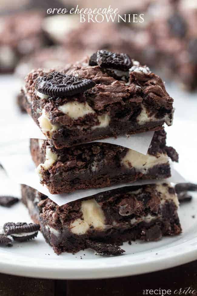 Oreo cheesecake brownies stacked on each other with a square cut out of parchment paper. 