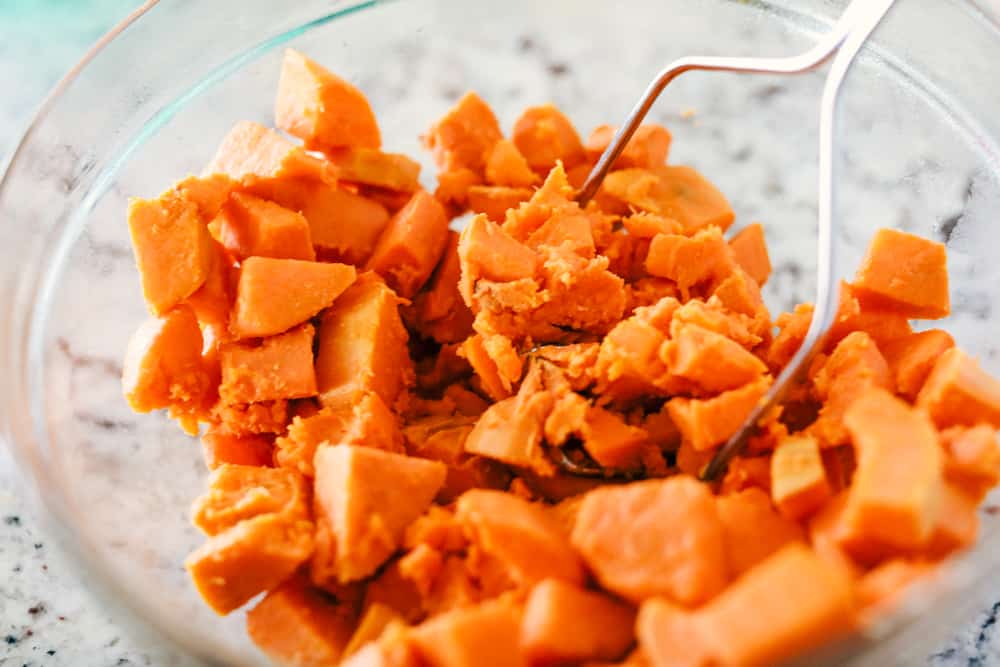 sweet potatoes being mashed in a bowl with a potato masher 