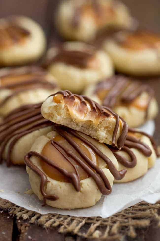 Twix thumbprint cookies stacked on each other on parchment paper with one of the cookies has a bite taken out of it. 