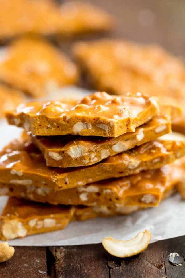 Cashew Brittle stacked on top of each other and on parchment paper. 