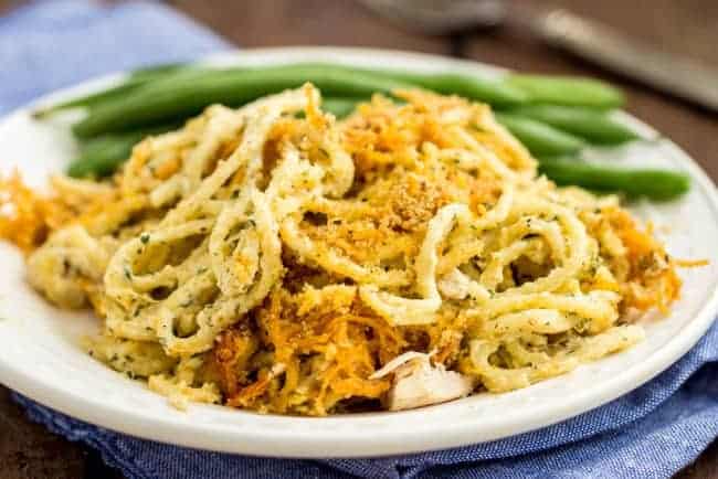 Cheesy Cheddar Chicken Spaghetti Casserole on a white plate with green beans on the side. 