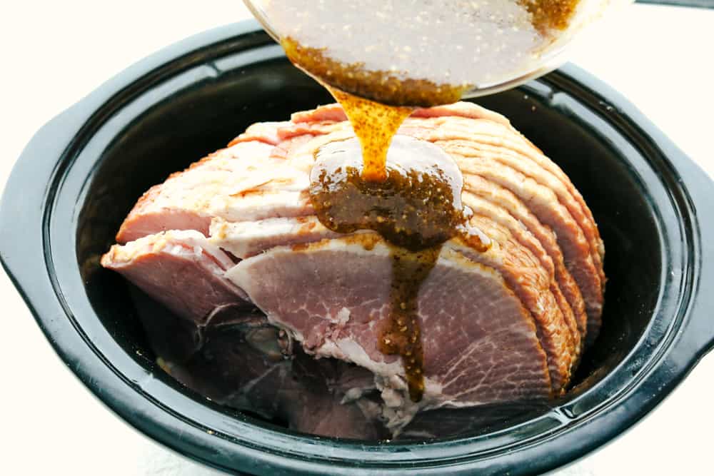 Pouring honey, mustard, and garlic glaze over the ham in a crock pot. 