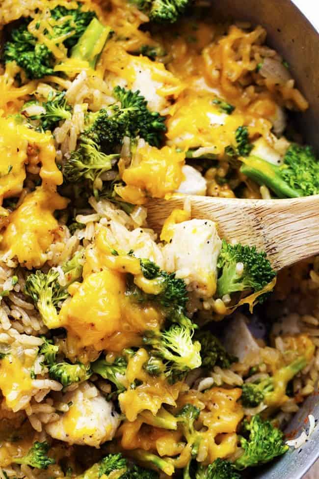 Cheesy chicken broccoli being stirred in a pot by a wooden spoon.