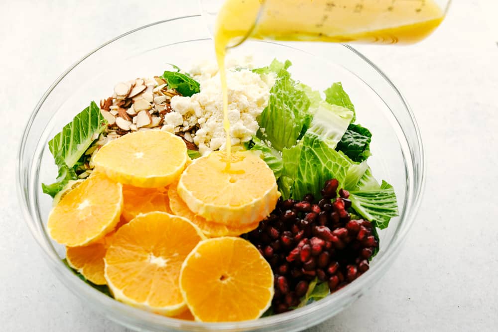 Pouring Orange Vinaigrette dressing over the salad.