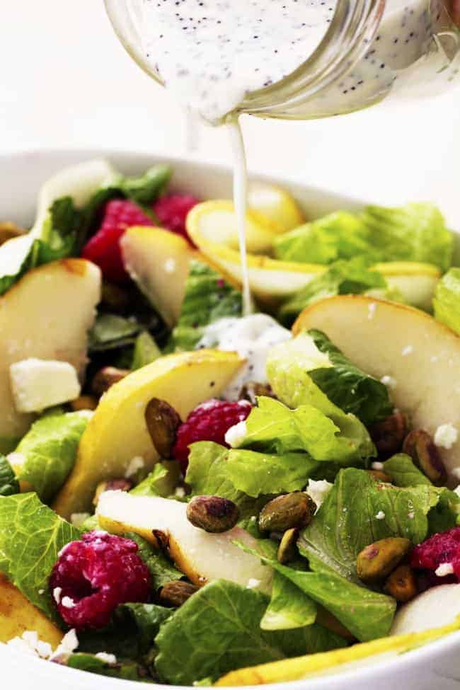 Pouring dressing on pear raspberry pistachio salad.