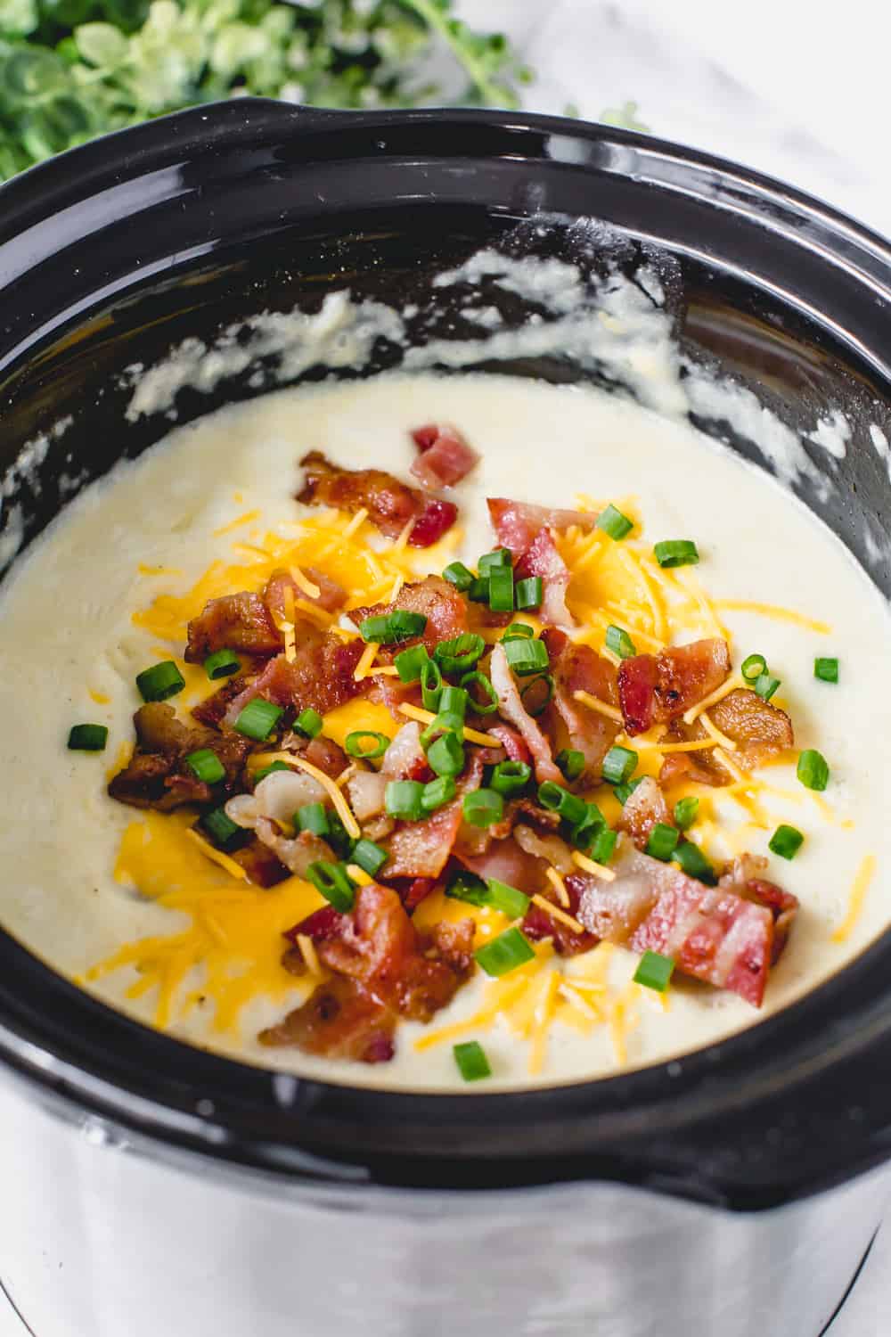 Slow cooker loaded baked potato soup in a slow cooker garnished with chopped bacon, cheese and onions. 