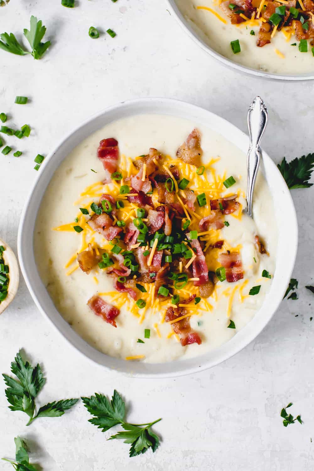 Cargado sopa de papa al horno en un tazón blanco con una cuchara adornada con tocino picado, queso y cebolla. 