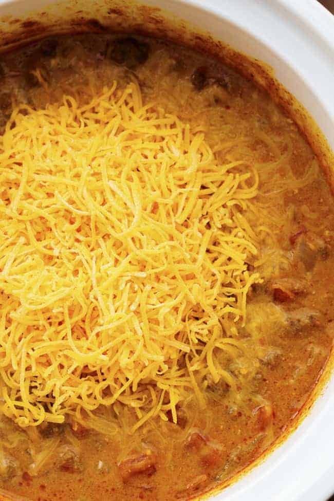 Slow cooker beefy nacho soup in a white pot, topped with shredded cheese.
