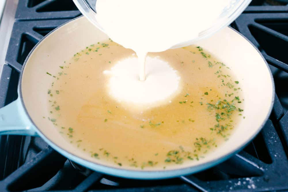 Milk pouring into a skillet of chicken broth and seasonings.
