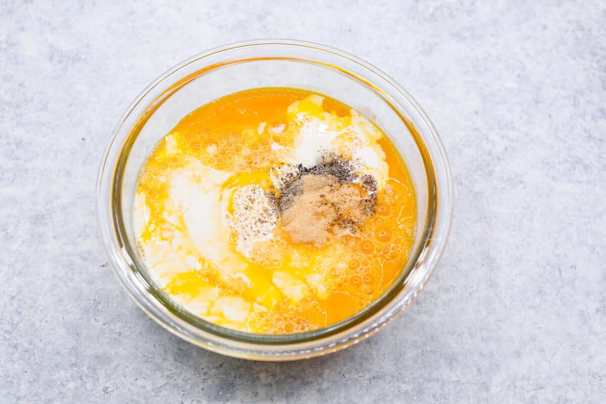 Overhead shot of eggs, milk, cream, salt, pepper and garlic powder in a small glass bowl. 