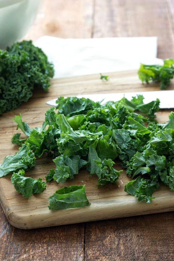 Kale being chopped on a wooden cutting board.