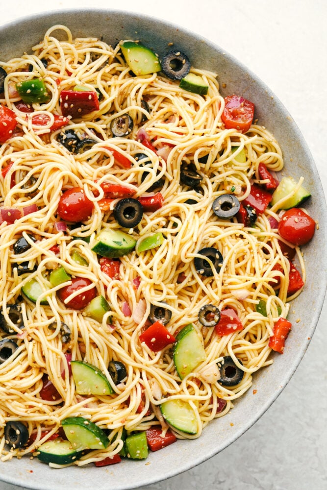 A colorful bowl of Italian pasta salad with rotini, fresh vegetables, and pasta salad dressing, surrounded by ingredients for tuna pasta salad and vegan pasta salad.