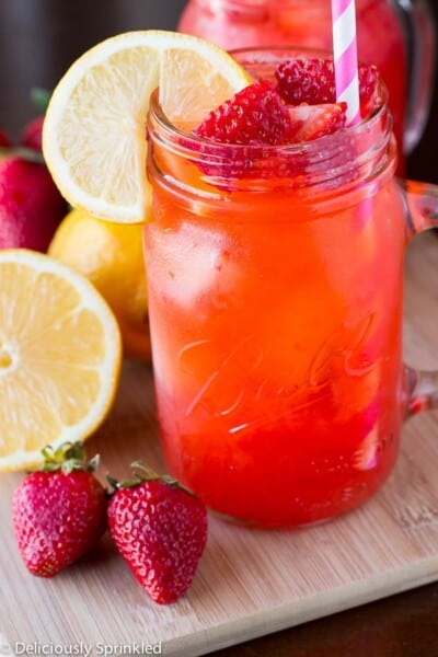 Fresh-Strawberry-Lemonade in a glass jar with strawberries and lemons and a pink and white straw.