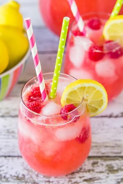 Raspberry lemonade with raspberry and lemon and yellow and lime green straws.